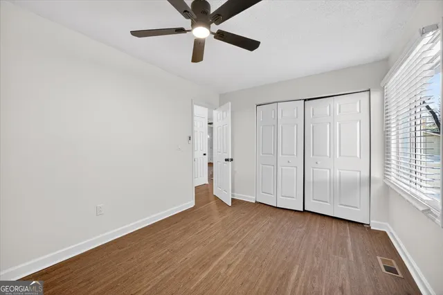 an empty room with wooden floor chandelier fan and windows