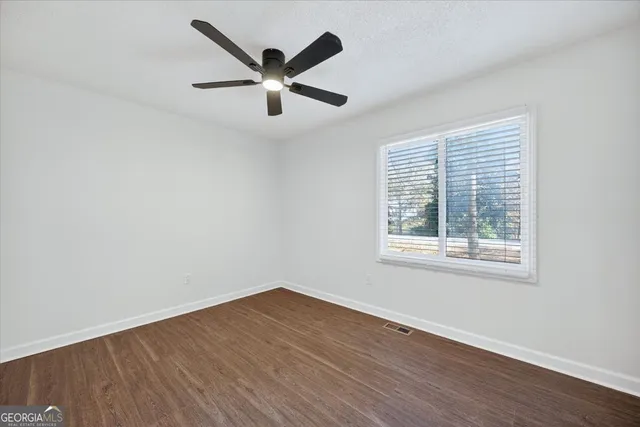 an empty room with wooden floor fan and windows