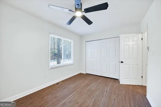 an empty room with wooden floor ceiling fan and windows