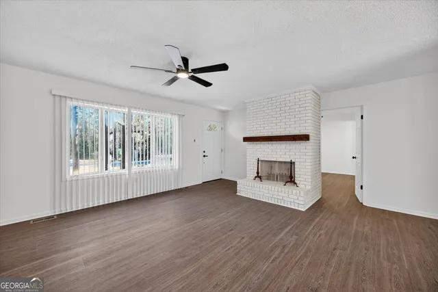 a view of an empty room with wooden floor fireplace and a window