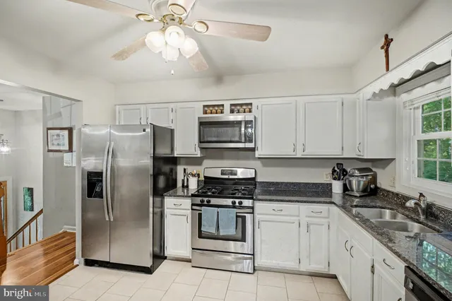 a kitchen with stainless steel appliances granite countertop a stove a sink dishwasher and white cabinets with wooden floor