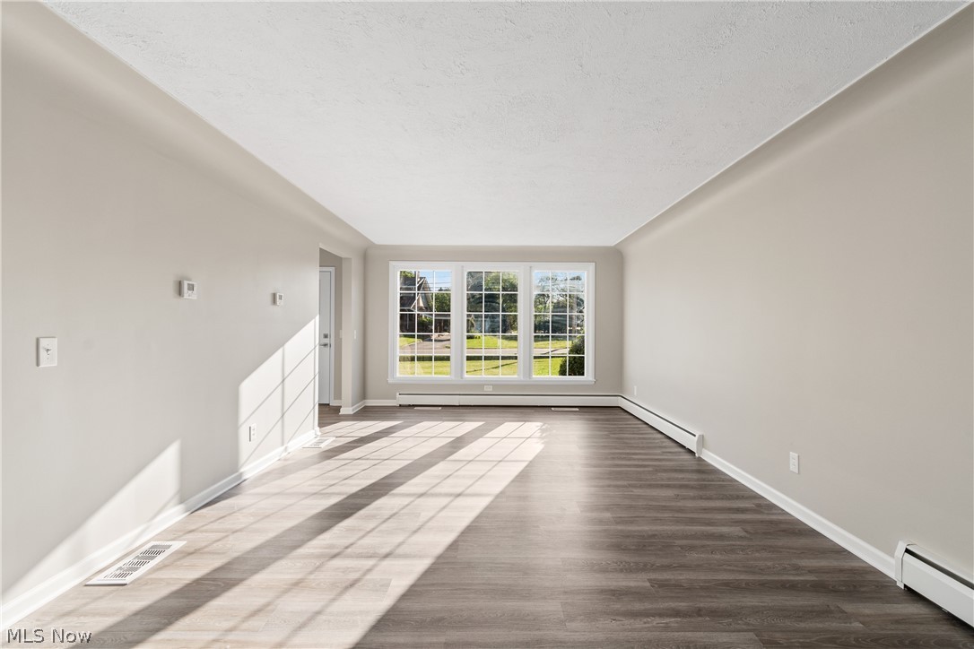 Unfurnished living room featuring hardwood / wood-style flooring, baseboard heating, and a textured ceiling