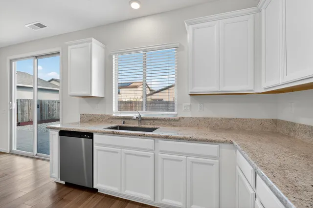 a kitchen with granite countertop stainless steel appliances white cabinets sink and window
