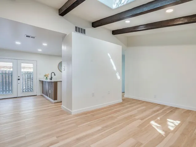 a view of an empty room with wooden floor and a kitchen view