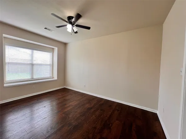 an empty room with wooden floor chandelier fan and windows