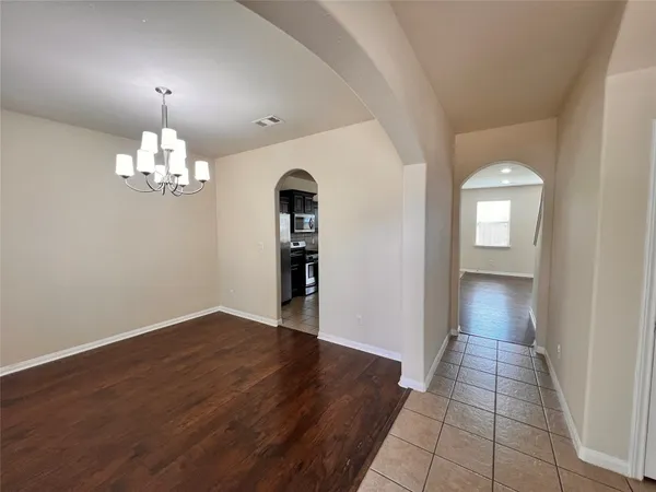 an empty room with wooden floor chandelier and windows