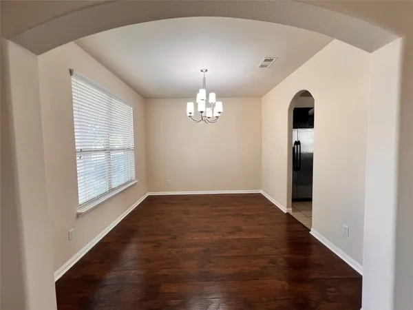an empty room with wooden floor chandelier and windows