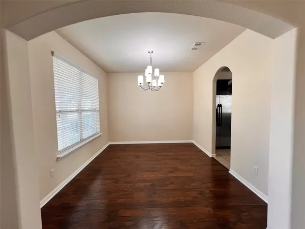 an empty room with wooden floor chandelier and windows