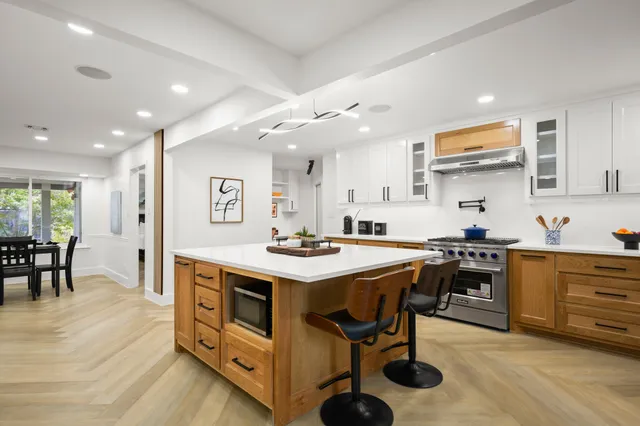 a kitchen with stainless steel appliances granite countertop a stove top oven a sink a dining table and chairs with wooden floor