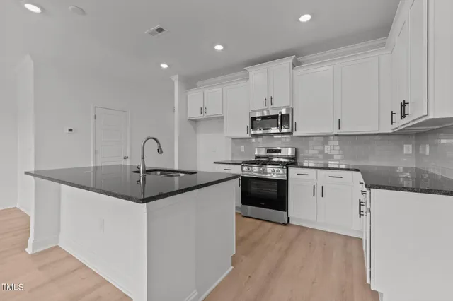 a kitchen with stainless steel appliances granite countertop a sink a stove a refrigerator and white cabinets