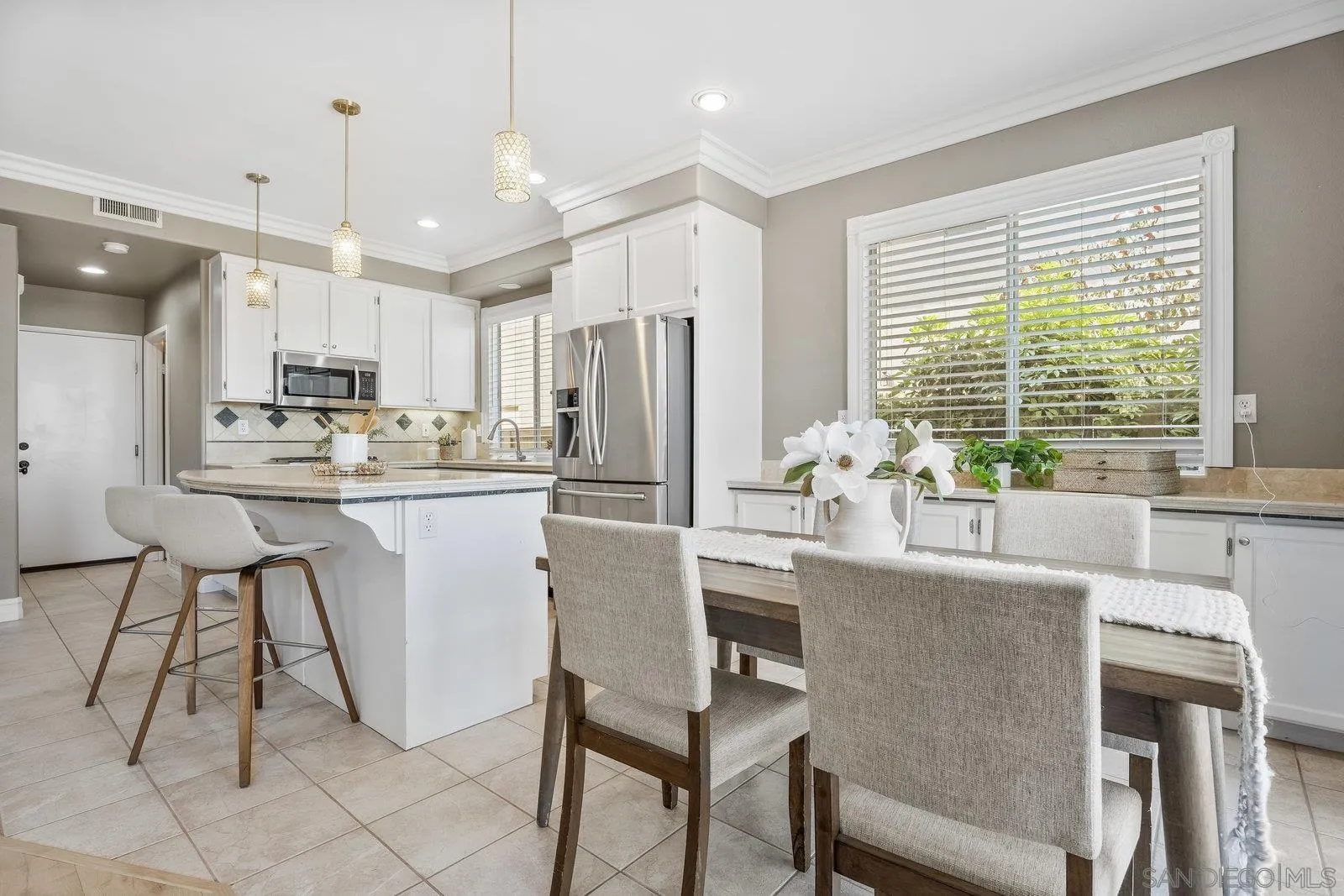 11542 Village Ridge Road San Diego, CA 92131 - Photo 12 of 42 a kitchen with stainless steel appliances kitchen island granite countertop a dining table chairs and white cabinets