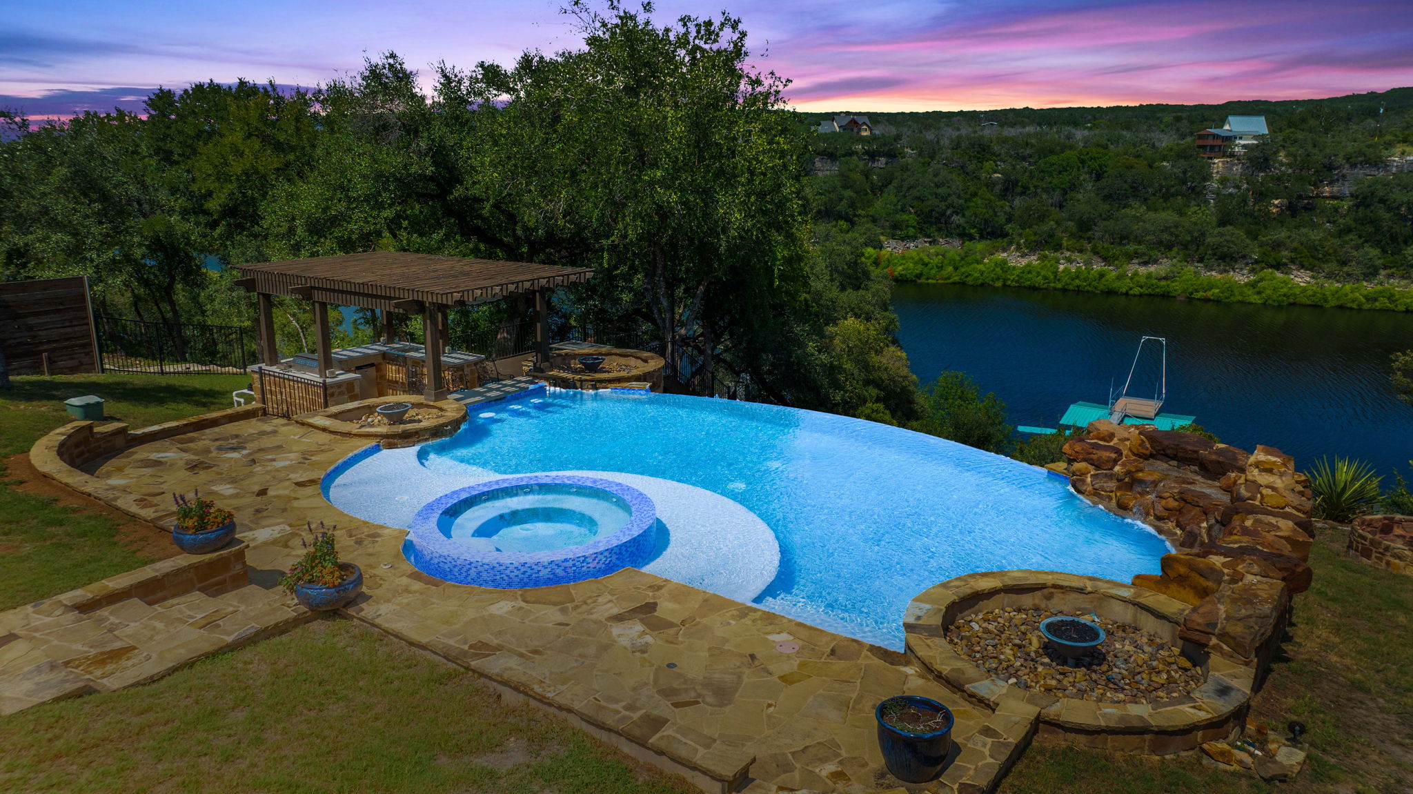 1325 Likeness Road Spicewood, TX 78669 - Photo 5 of 40 Pool at dusk with a pool with connected hot tub, a patio area, a water view, and a lawn