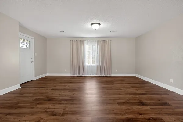 a view of an empty room with wooden floor and window