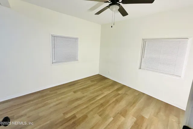 a view of empty room with wooden floor and fan