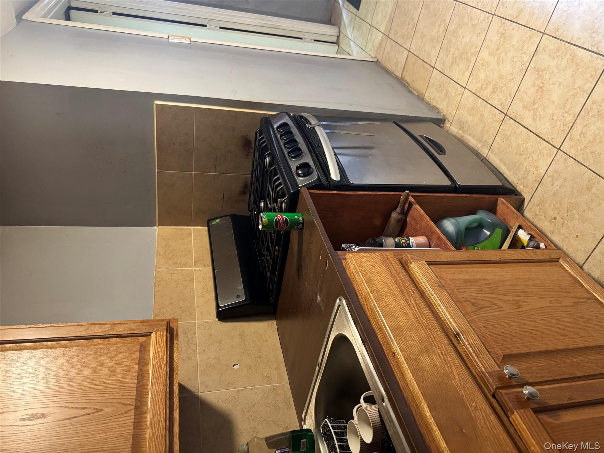 94-13 116th Street Queens, NY 11419 - Photo 32 of 34 Kitchen featuring stainless steel gas stove, dark countertops, brown cabinets, light tile patterned floors, and backsplash