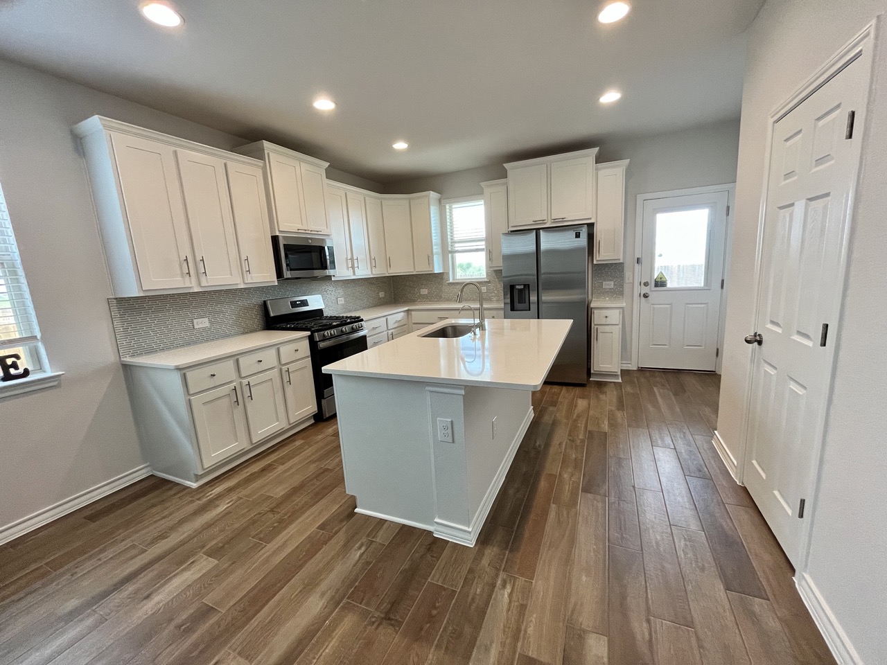 11715 Caithness Way Austin, TX 78653 - Photo 11 of 40 Kitchen featuring stainless steel appliances, white cabinetry, backsplash, a kitchen island with sink, and recessed lighting