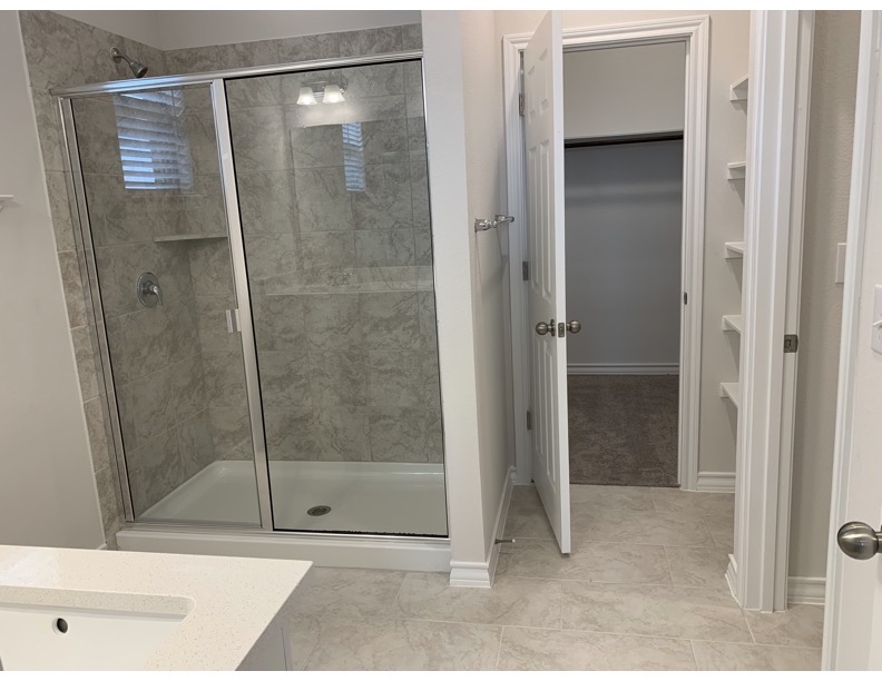 11715 Caithness Way Austin, TX 78653 - Photo 32 of 40 Primary bathroom featuring a stall shower, a walk in closet, vanity, and light tile patterned floors