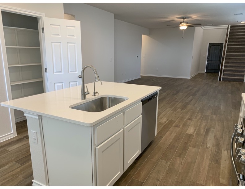 11715 Caithness Way Austin, TX 78653 - Photo 7 of 40 Kitchen featuring dark wood-style floors, an island with sink, stainless steel appliances, white cabinets, and light stone counters
