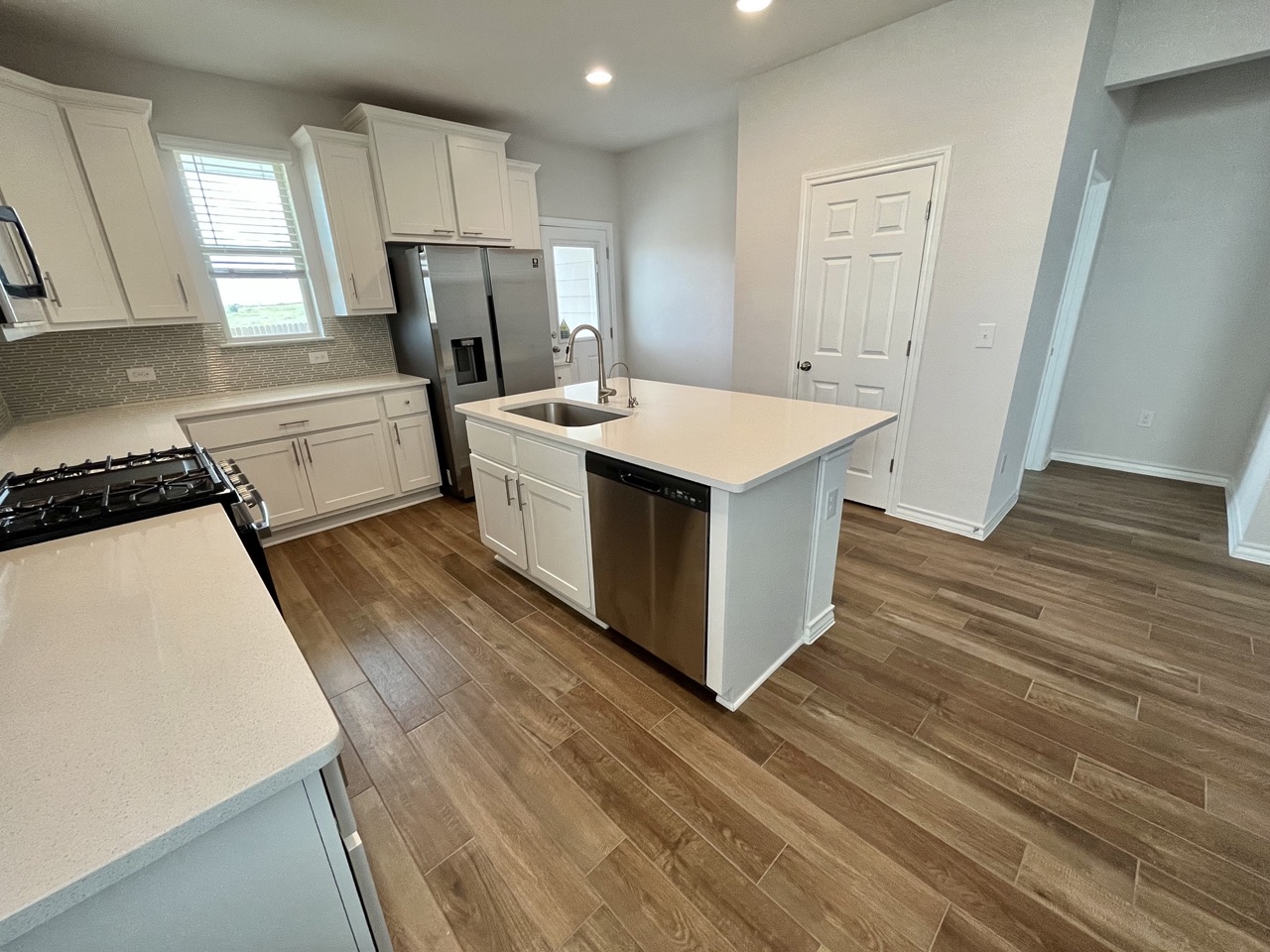 11715 Caithness Way Austin, TX 78653 - Photo 9 of 40 Kitchen with white cabinetry, backsplash, dark wood finished floors, stainless steel appliances, and a kitchen island with sink