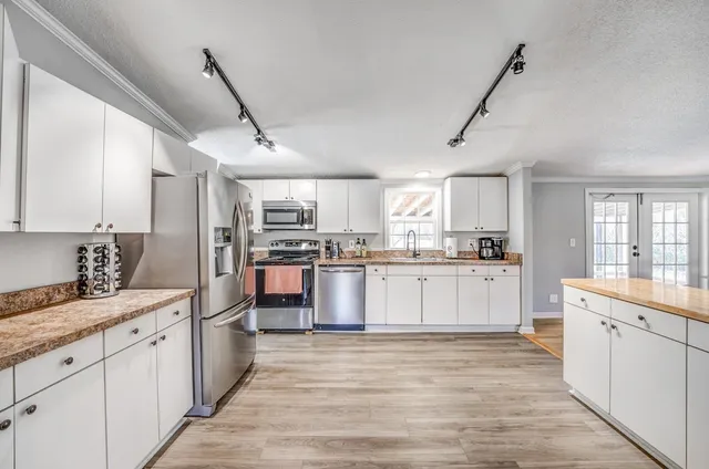 a large kitchen with stainless steel appliances kitchen island granite countertop a stove a sink a refrigerator and white cabinets with wooden floor