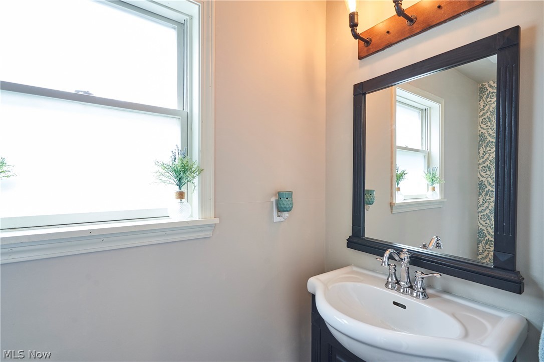 780 Bates Road Rocky River, OH 44116 - Photo 22 of 35 Bathroom featuring a wall-mounted mirror with a dark frame, a vanity with an integrated sink, polished chrome faucet, and a window with white trim