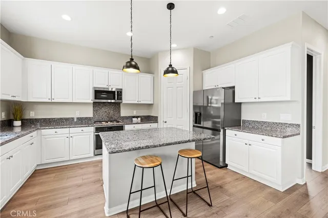 a kitchen with stainless steel appliances granite countertop a stove top oven a refrigerator a sink and white cabinets with wooden floor