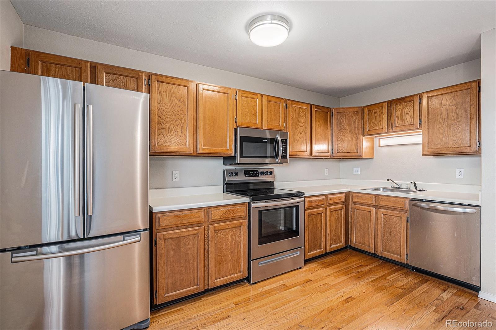 8915 Field Street, Unit 113 Westminster, CO 80021 - Photo 6 of 38 a kitchen with stainless steel appliances granite countertop a refrigerator a stove top oven a sink and dishwasher with wooden floor
