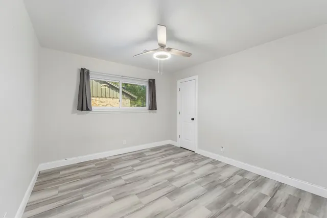 an empty room with wooden floor ceiling fan and windows