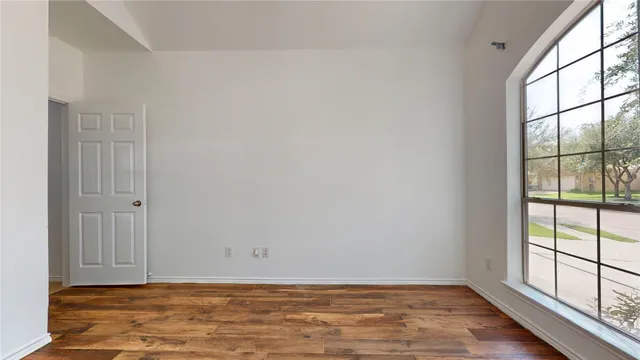 a view of an empty room with wooden floor and a window