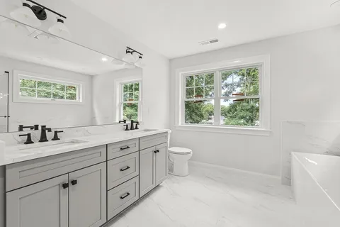 a bathroom with a granite countertop sink a large mirror a toilet and a window