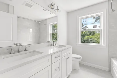 a bathroom with a granite countertop sink a large mirror a toilet and a window