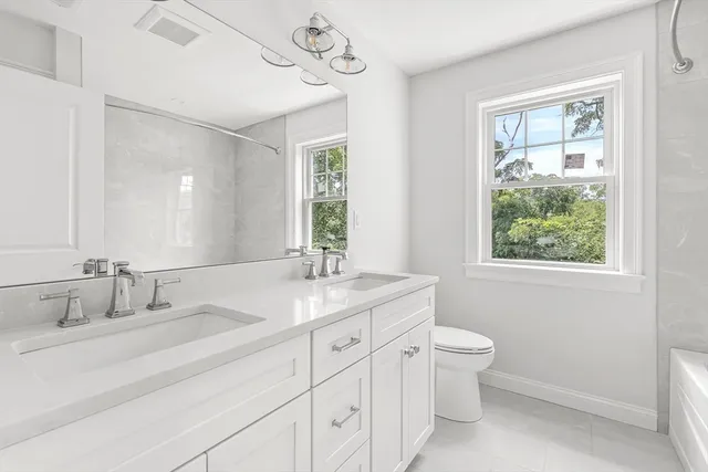 a bathroom with a granite countertop sink a large mirror a toilet and a window
