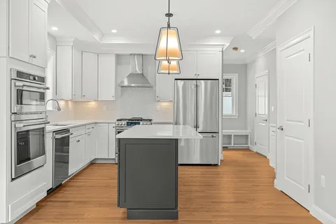 a kitchen with stainless steel appliances granite countertop a refrigerator a stove oven and white cabinets with wooden floors