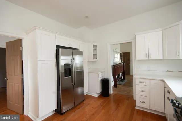 a kitchen with stainless steel appliances granite countertop a refrigerator a sink a stove and white cabinets with wooden floor