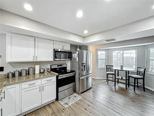 a kitchen with stainless steel appliances granite countertop a refrigerator a stove top oven a sink dishwasher a dining table and chairs with wooden floor