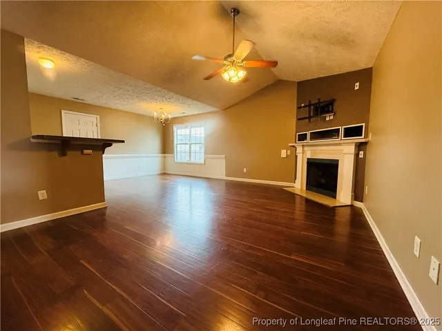 a view of an empty room with wooden floor and a kitchen