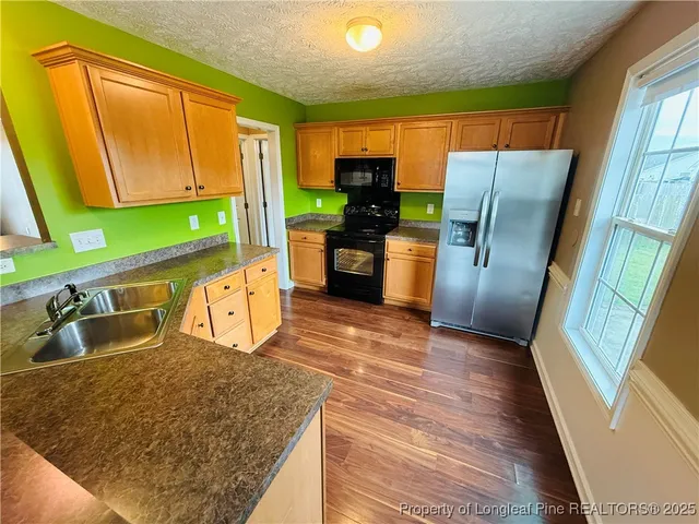a kitchen with stainless steel appliances granite countertop a refrigerator a stove and a sink with wooden floor