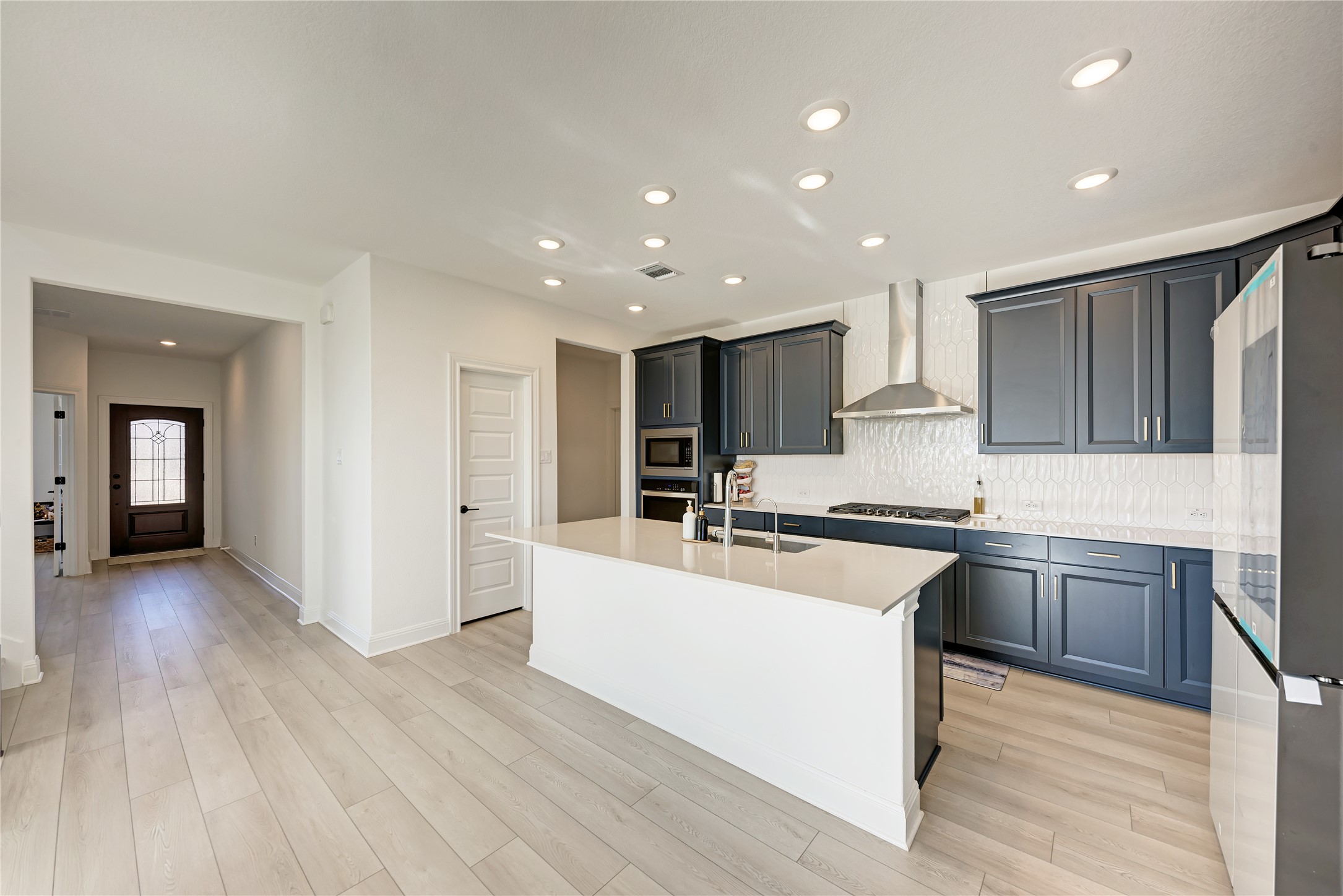 316 Regatta Trail Leander, TX 78641 - Photo 6 of 37 Contemporary kitchen featuring dark blue cabinetry, light wood-finish flooring, and a white countertop island