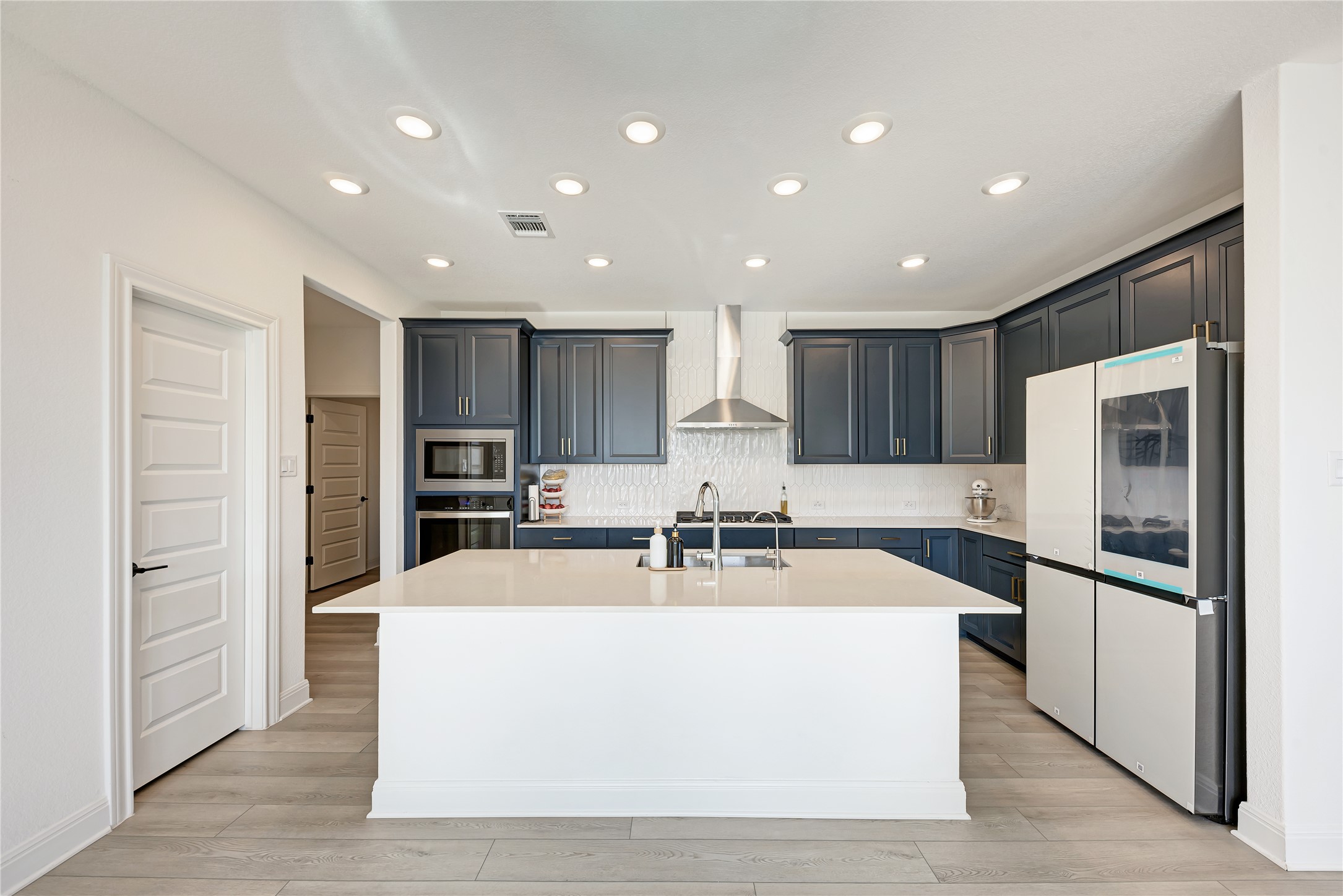 316 Regatta Trail Leander, TX 78641 - Photo 9 of 37 Modern kitchen featuring a central island with a sink, white quartz countertops, dark blue cabinetry, and wood-finish flooring