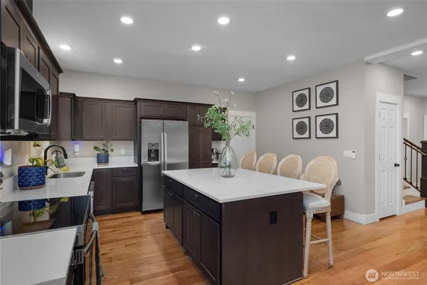 a kitchen with stainless steel appliances granite countertop a refrigerator a stove top oven a sink dishwasher and white cabinets with wooden floor