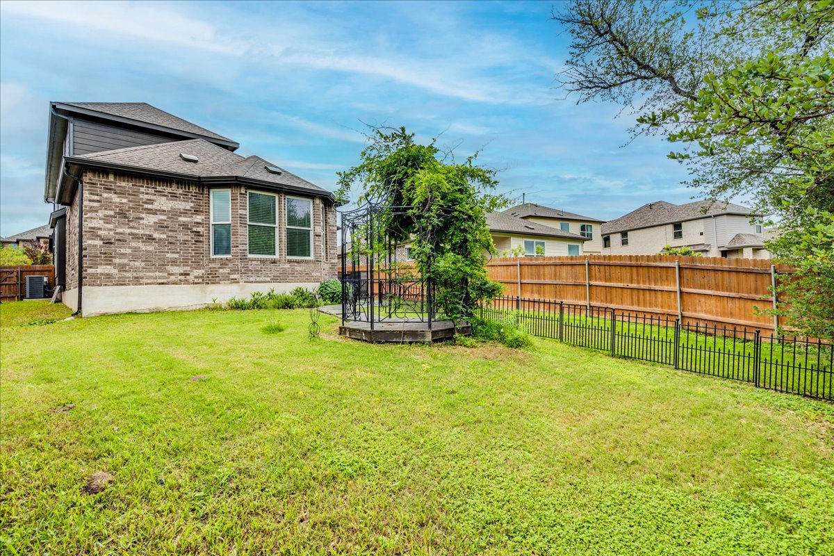 8008 Prairie Rye Drive Lago Vista, TX 78645 - Photo 31 of 40 Expansive backyard featuring a lush lawn, a decorative metal gazebo with climbing greenery, and a mix of wood and wrought iron fencing