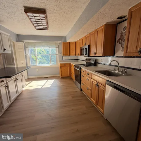 a large kitchen with stainless steel appliances a large counter top a stove a chimney wooden cabinets and a sink