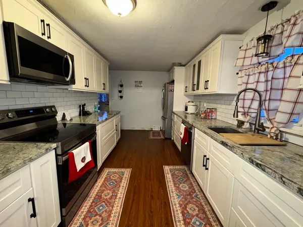 a kitchen with stainless steel appliances granite countertop a sink a stove top oven a chimney and cabinets