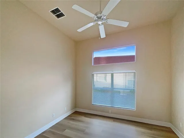an empty room with wooden floor fan and windows