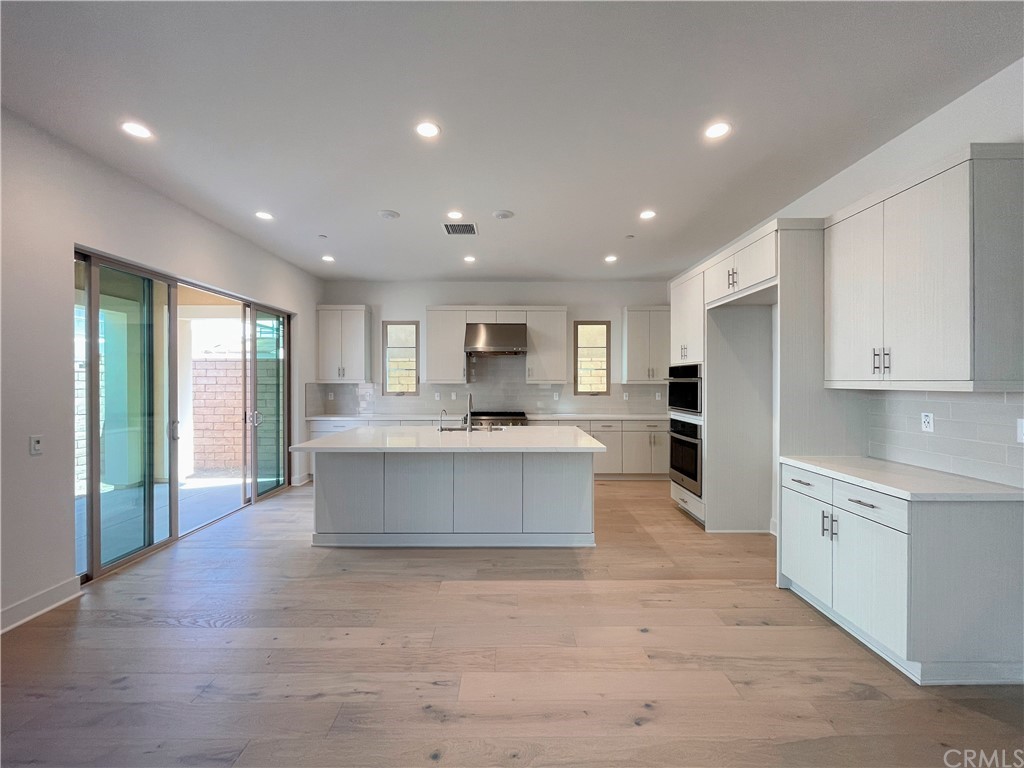 215 Sutters Mill Irvine, CA 92602 - Photo 19 of 57 a large white kitchen with kitchen island a sink wooden floor and a refrigerator