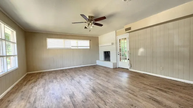 an empty room with wooden floor fan and windows