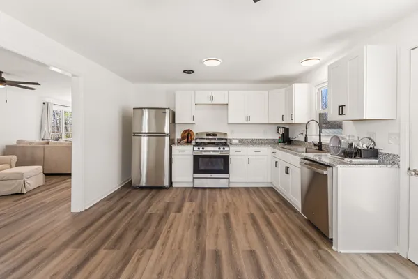 a kitchen with granite countertop a refrigerator oven a sink dishwasher and white cabinets with wooden floor