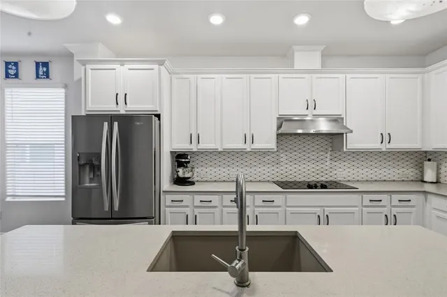 a kitchen with stainless steel appliances granite countertop a refrigerator a sink and white cabinets