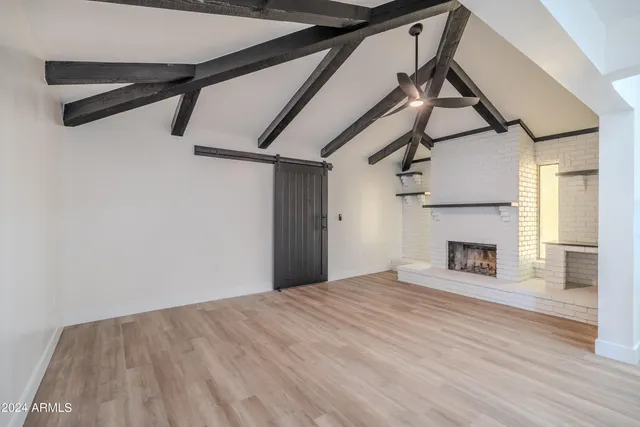 a view of an empty room with wooden floor fireplace and a window