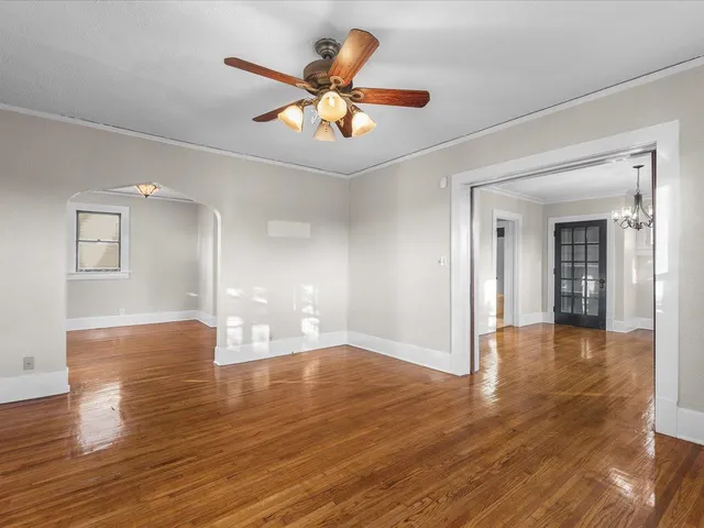 a view of an empty room with wooden floor and a ceiling fan